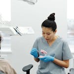 Dental professional demonstrating brushing or denture care on a teeth model for a seated patient in a clinic.