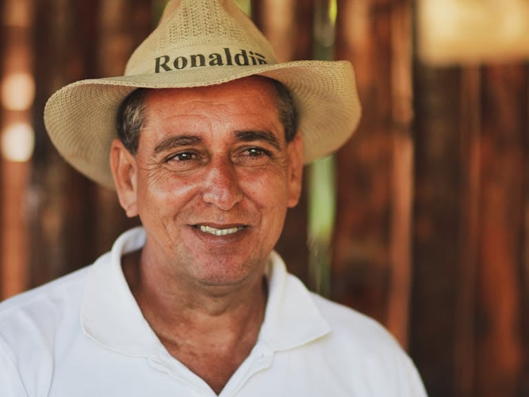 Smiling middle-aged man wearing a straw hat and white collared shirt.