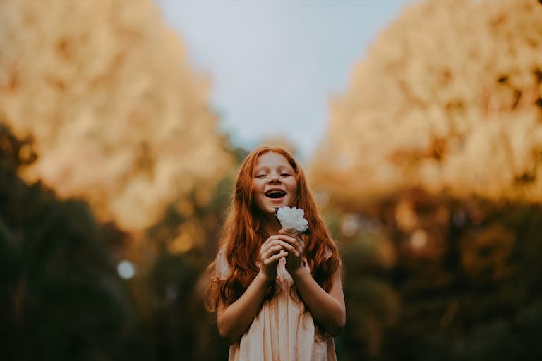 Smiling redheaded child holding a white flower outdoors.