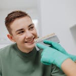 Smiling teenage boy during a dental shade comparison with a dentist holding a tooth shade guide.