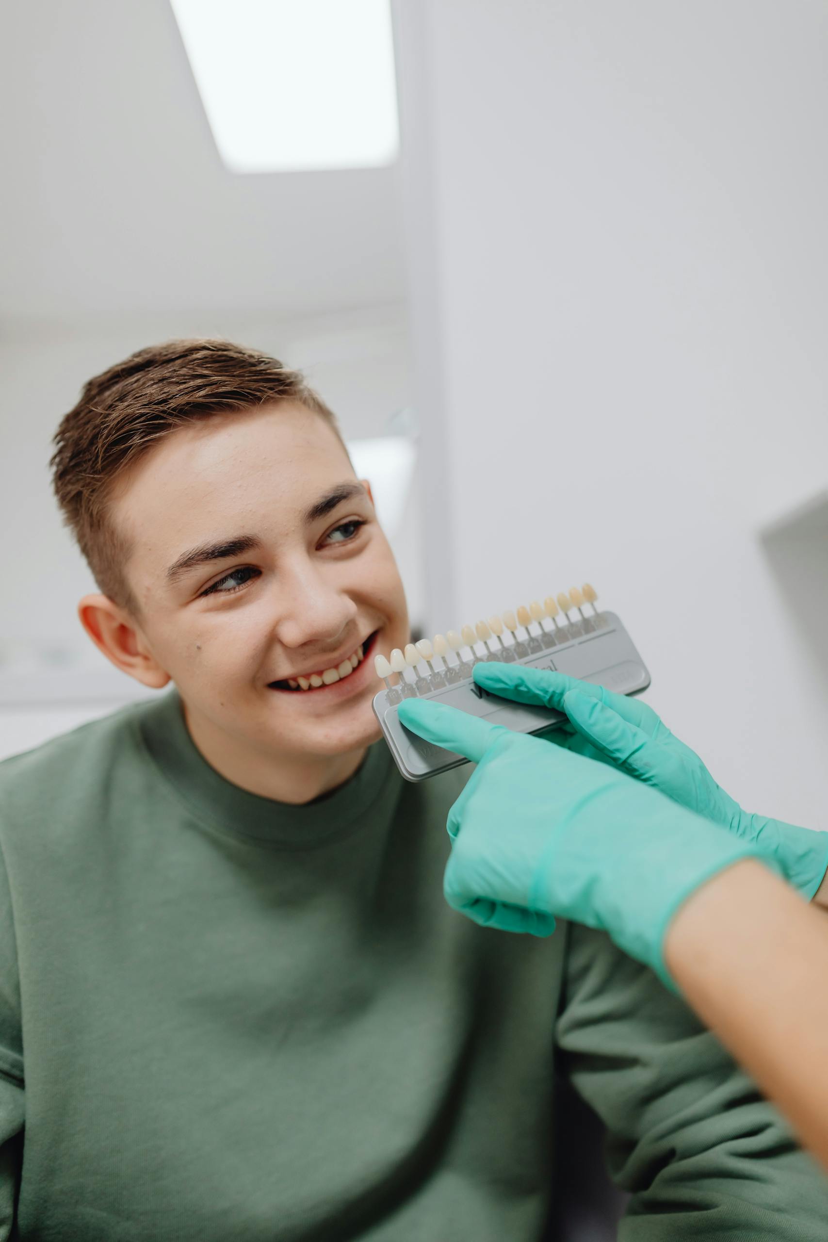 Smiling teenage boy during a dental shade comparison with a dentist holding a tooth shade guide.