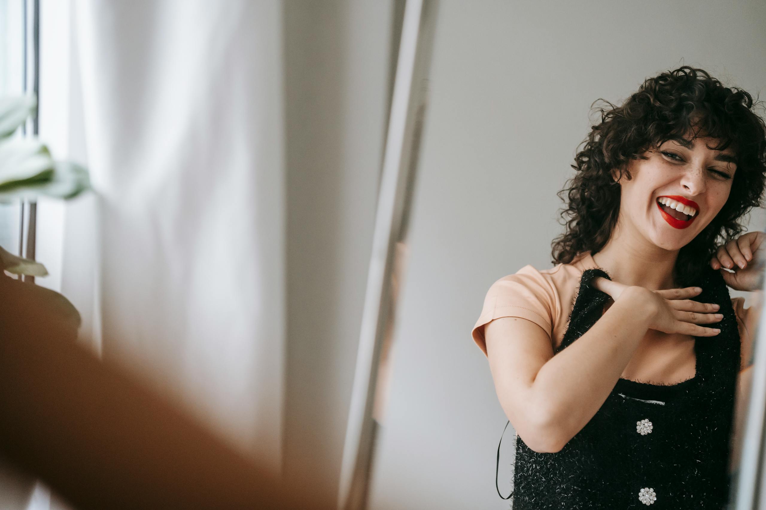 Smiling woman with curly hair looking at her reflection in a mirror at home.