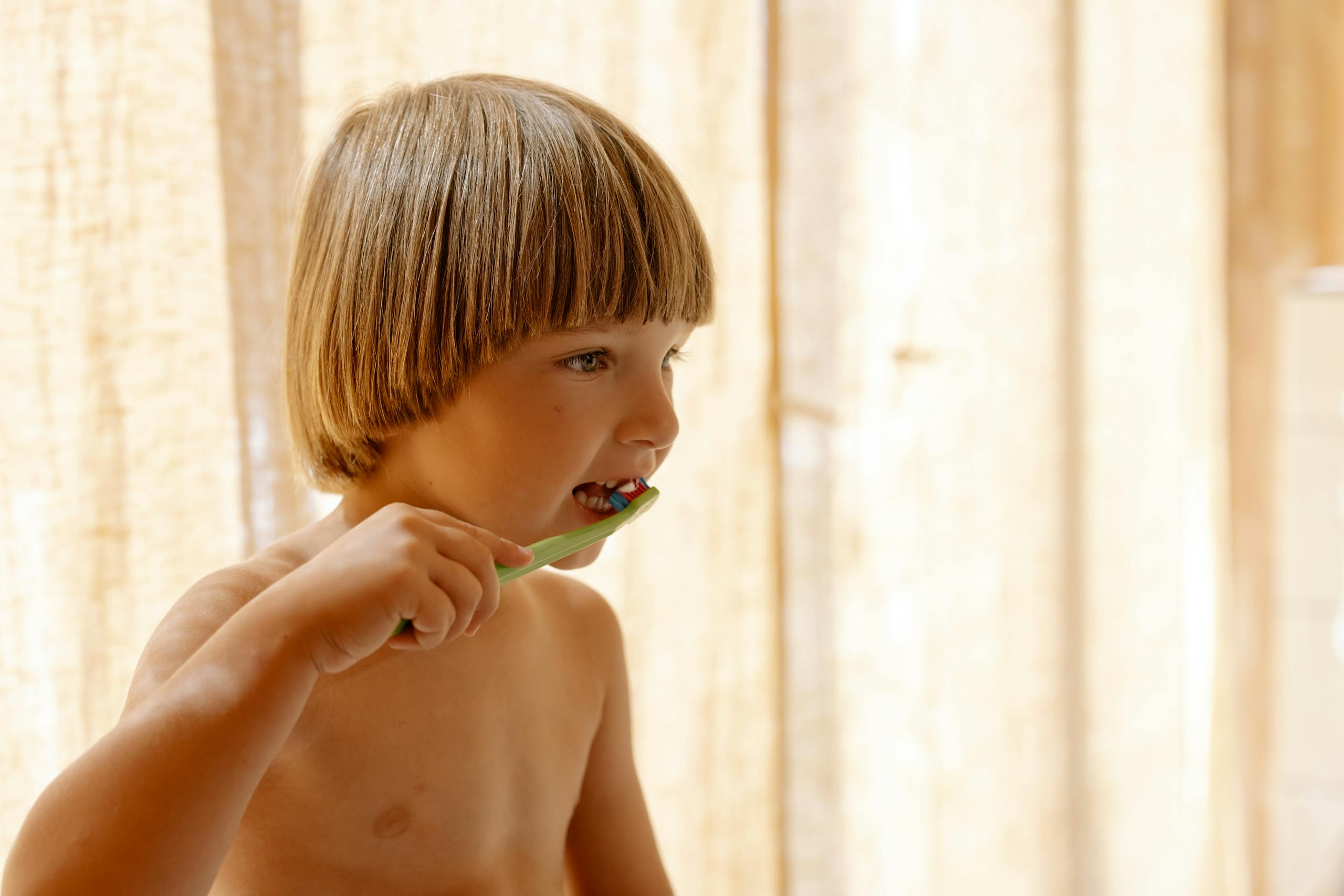 Young boy brushing his teeth indoors in soft natural light.