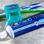 Close-up of toothbrushes, dental floss, and a toothpaste tube on a countertop.
