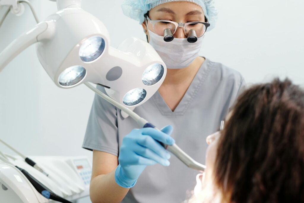 Dentist examining a patient with dental tools and overhead exam light in a modern clinic.