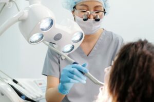 Dentist examining a patient with dental tools and overhead exam light in a modern clinic.