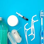 Flat lay of oral hygiene items on a blue surface, including mouthwash, floss picks, a floss container, and toothbrushes.
