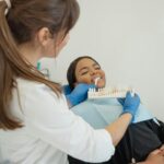 Dentist comparing a tooth shade guide with a smiling patient in a dental chair.