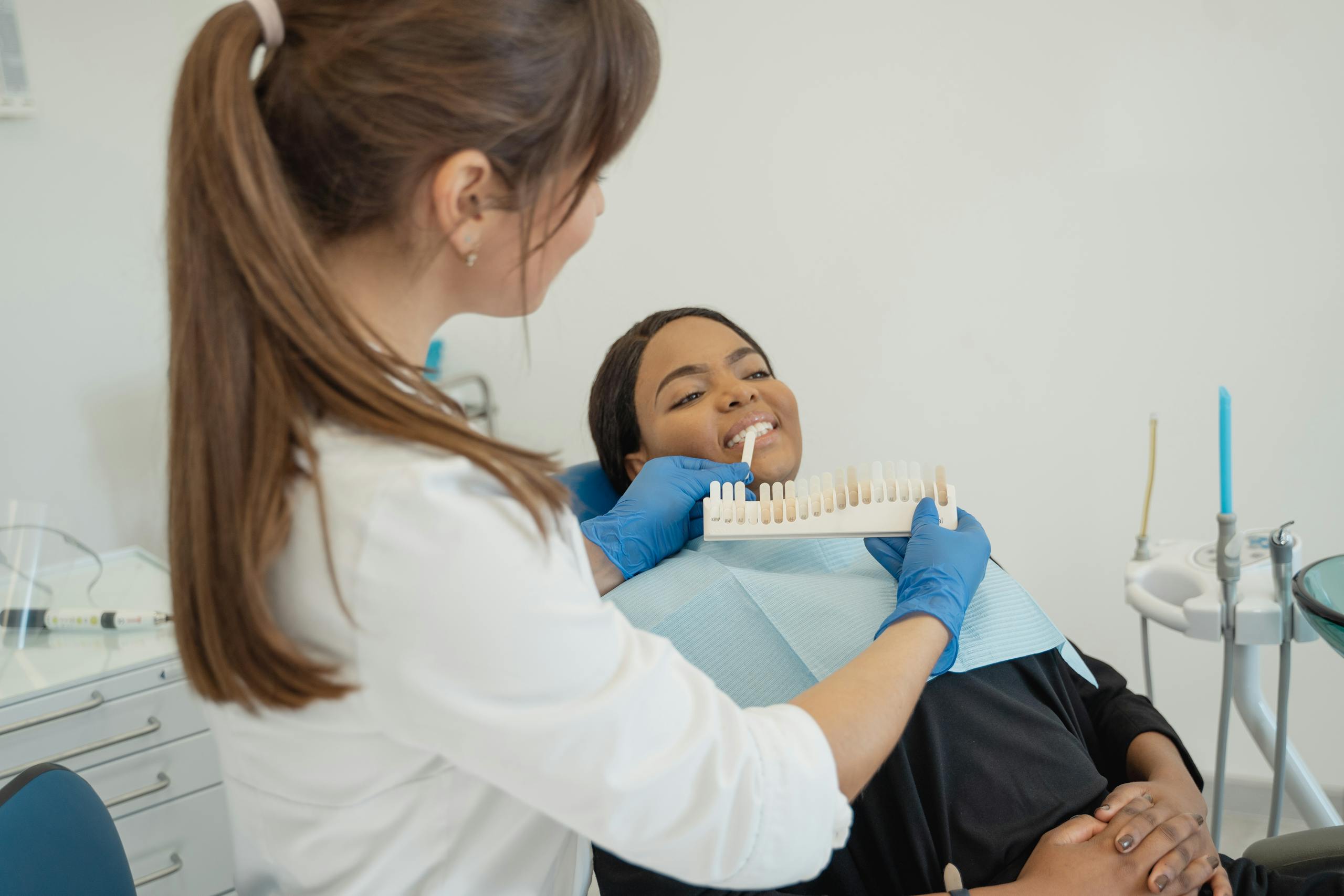 Dentist comparing a tooth shade guide with a smiling patient in a dental chair.