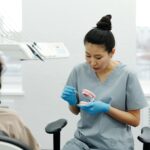 Dental professional demonstrating brushing or denture care on a teeth model for a seated patient in a clinic.