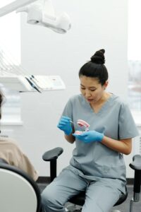 Dental professional demonstrating brushing or denture care on a teeth model for a seated patient in a clinic.